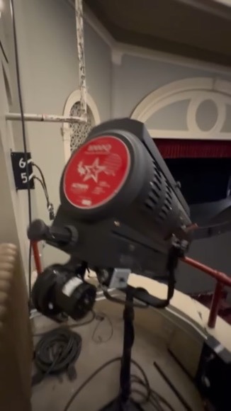 A stage light rigged above the East High School auditorium, marked with the school's red Angel emblem