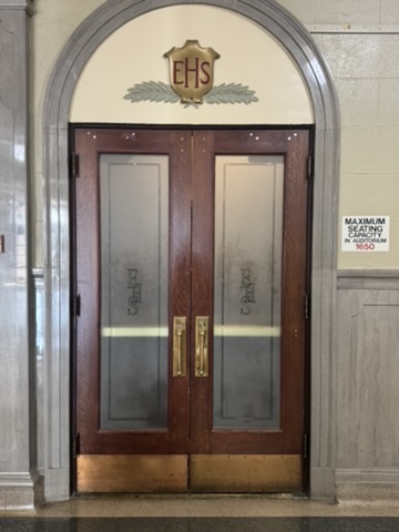 Wooden auditorium doors at East High School beneath a carved EHS crest set in a stone arch