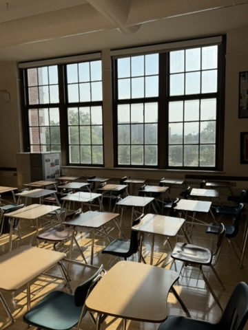 An East High School classroom filled with daylight from a wall of tall windows, desks arranged in rows