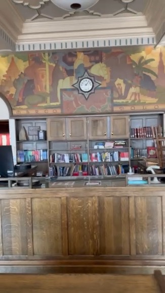 The historic painted mural and clock above the wooden circulation desk in the East High School library